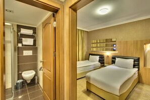 Habitación de hotel con puerta de madera, ducha, inodoro, cama y mesita de noche con lámpara.