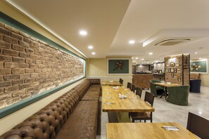 Un restaurant avec un mur en briques, de longues tables en bois et des bancs rembourrés.