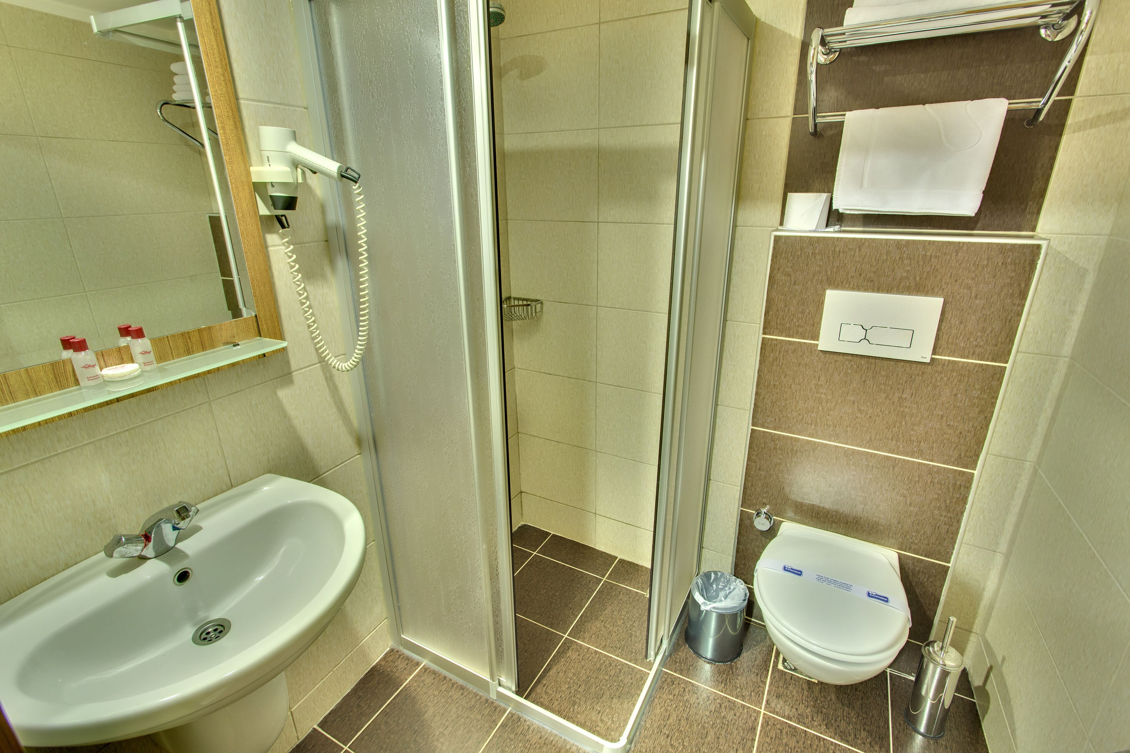 Un baño con ducha, lavamanos, inodoro y un perchero para toallas.