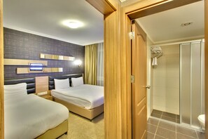 Habitación de hotel con dos camas, ducha y televisor montado en la pared.