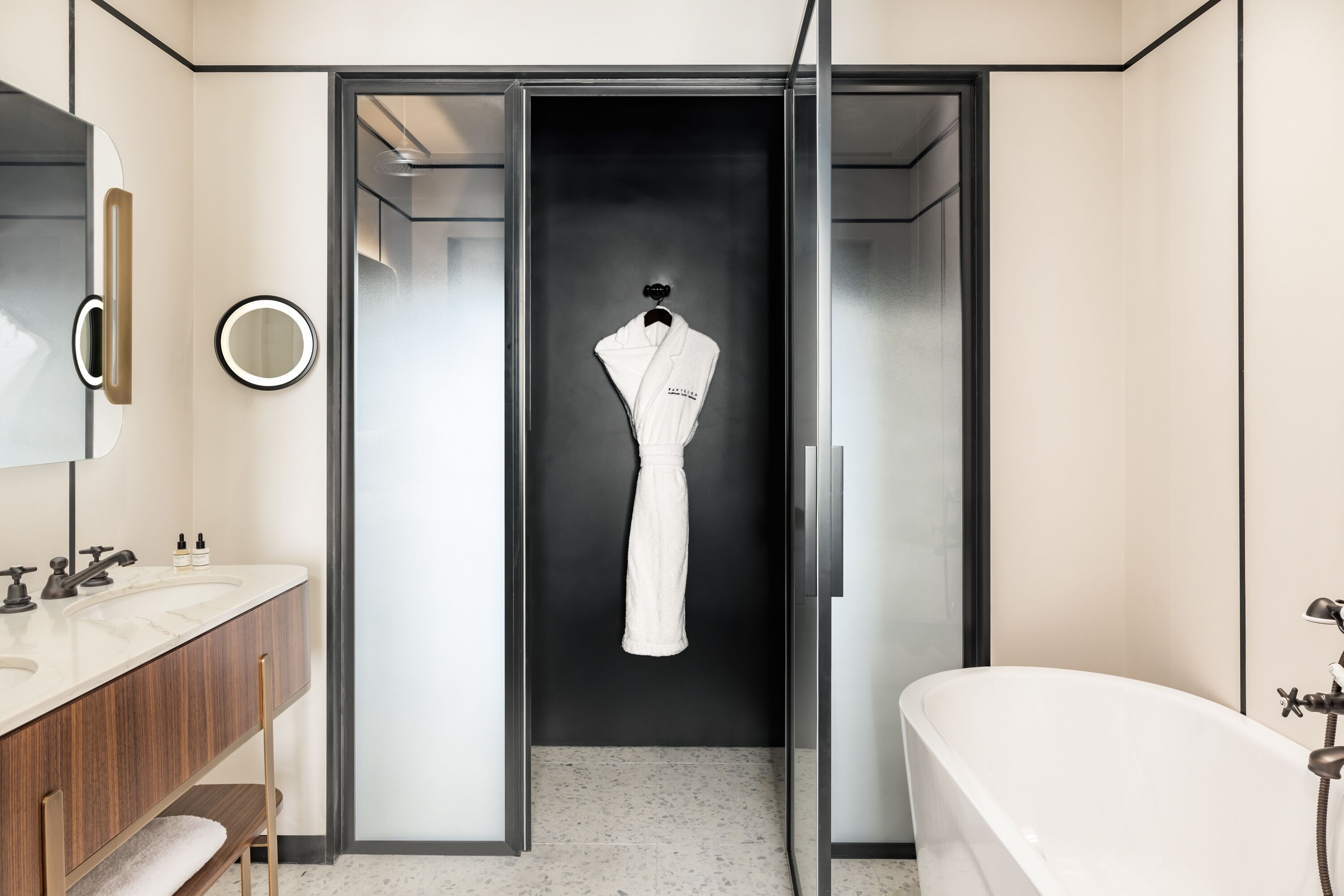 A modern bathroom with a large mirror, a white bathtub, and a robe hanging on a door.