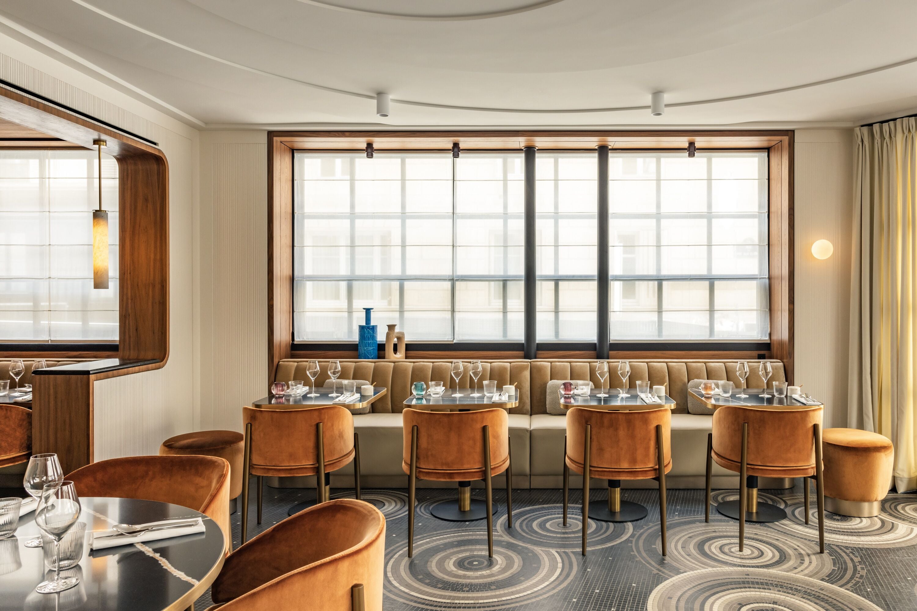 Un espace de restauration d’hôtel doté d’une grande fenêtre, de tables rondes et de sièges rembourrés.