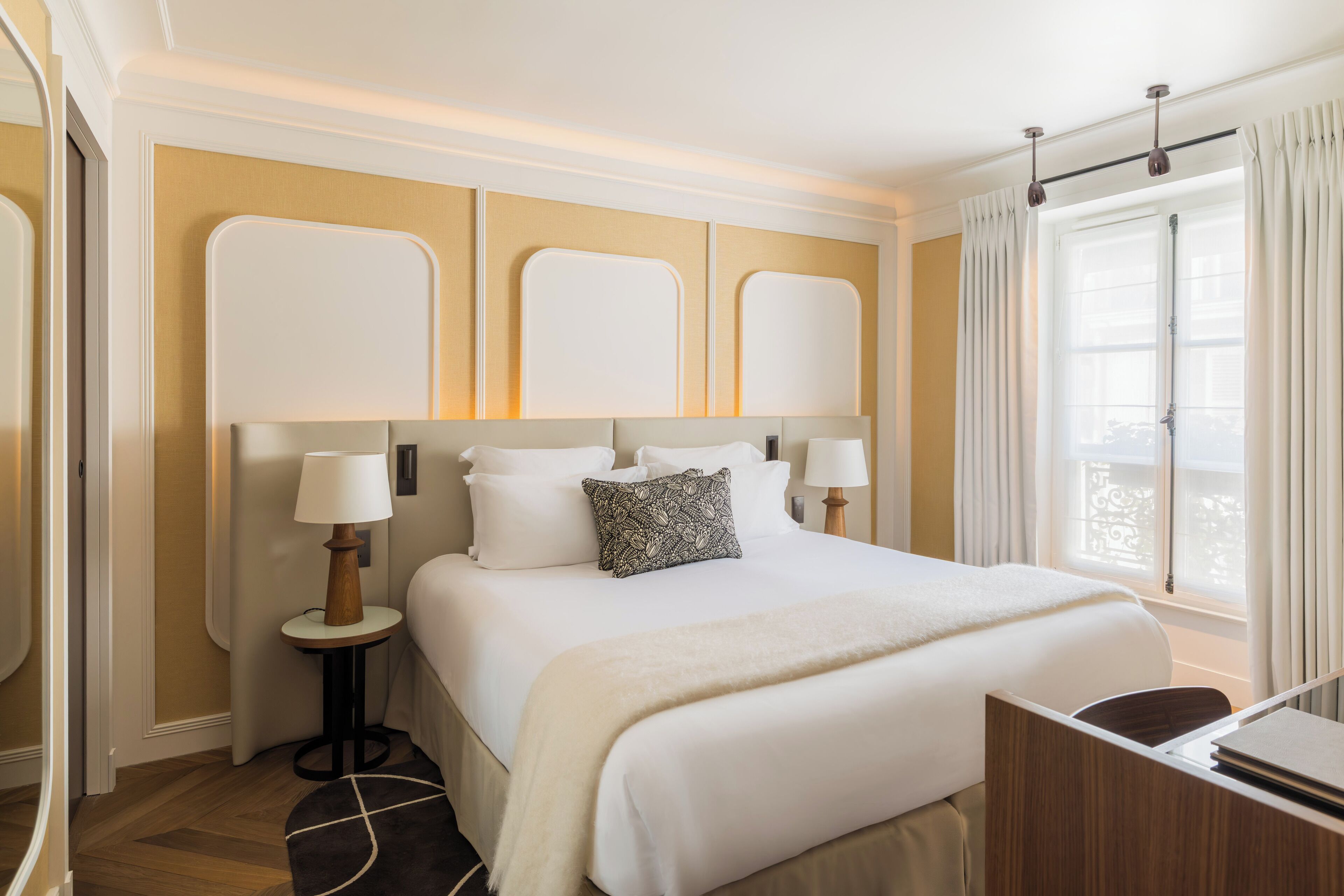 Een hotelkamer met een groot bed, twee nachtkastjes met lampen, een raam met gordijnen en een houten vloer.