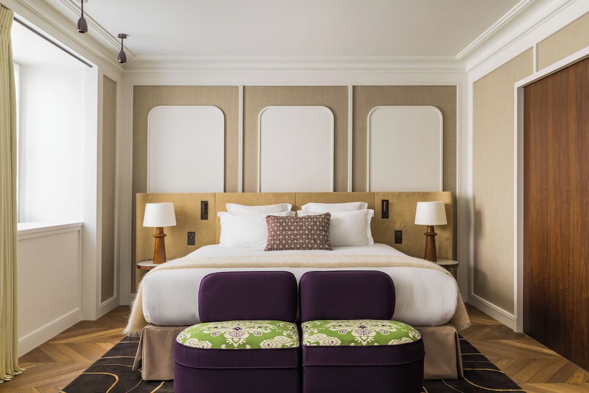 Habitación de hotel con una cama grande, dos lámparas de noche, un cabecero de madera y una ventana con cortinas.