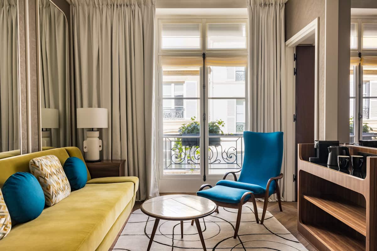 Una sala de estar moderna con un sofá amarillo, un sillón azul, una mesa de centro redonda y un aparador de madera.