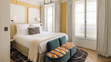 Una habitación de hotel con cama, un banco, una ventana con cortinas y una lámpara.