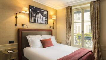 Habitación de hotel con una cama grande, dos lámparas de pared, un cuadro enmarcado sobre la cama y una ventana con cortinas.