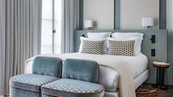 A bedroom with a large bed, two bedside lamps, a nightstand, and a patterned ottoman.