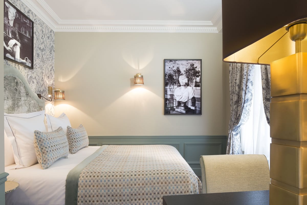 Habitación de hotel con cama, dos lámparas fijadas a la pared, una fotografía enmarcada y una mesa con una silla.