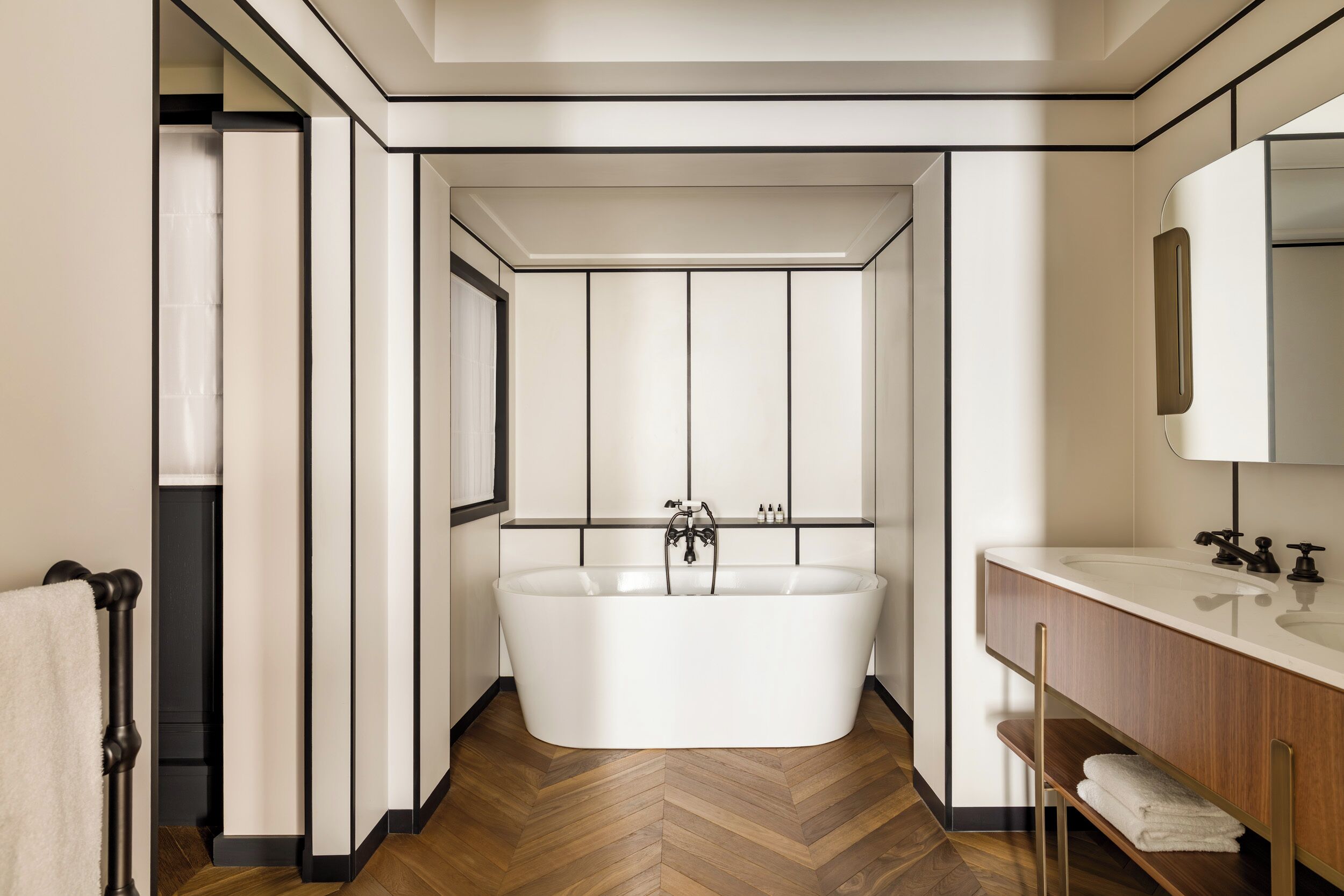 Ein modernes Badezimmer mit einer freistehenden Badewanne, einem Waschtisch mit Spiegel und einem Fischgrätenparkettboden.