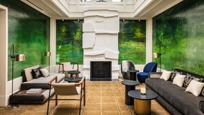 A modern interior with a fireplace, seating area, and large windows with green foliage views. - Pavillon Faubourg Saint-Germain & Spa (Paris)