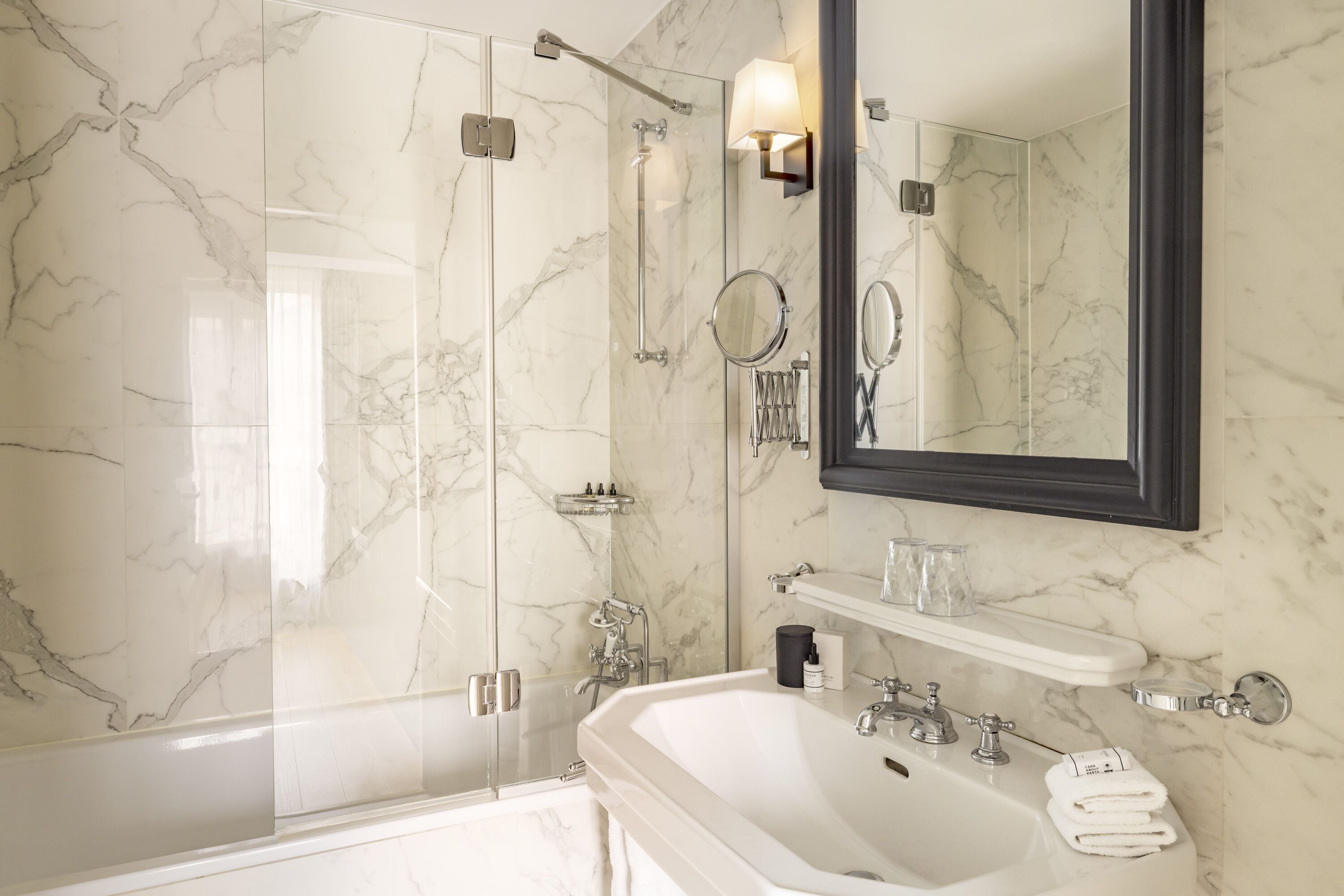 A modern bathroom with a glass-enclosed shower, a large mirror, and a white sink with a towel rack.