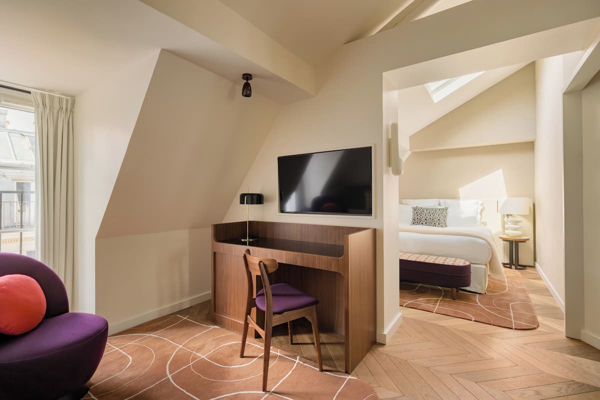 Habitación de hotel con escritorio, silla, televisor, cama y vista a la ciudad.