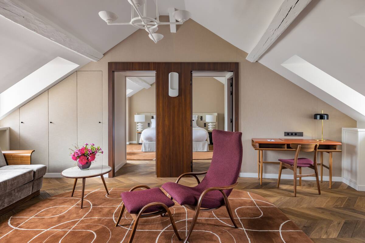 Amplio dormitorio tipo loft con techo inclinado, un escritorio de madera, un sillón morado y una pequeña mesa redonda con un florero.