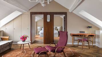 A spacious loft bedroom with a sloped ceiling, a wooden desk, a purple armchair, and a small round table with a vase of flowers.