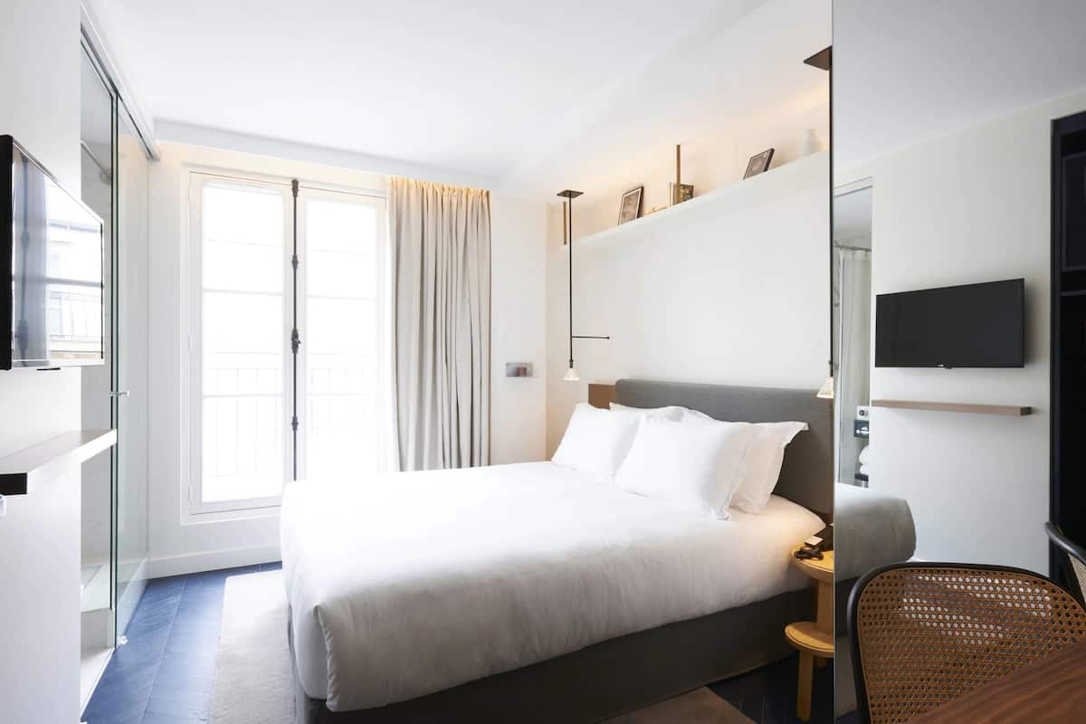 Una habitación de hotel moderna con una cama grande, un televisor, una mesita y una silla.