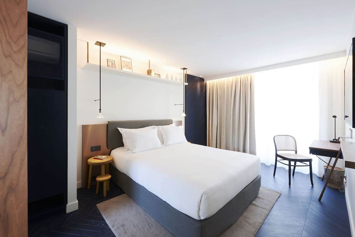 Una habitación de hotel moderna con una cama grande, un escritorio, una silla y un taburete pequeño.