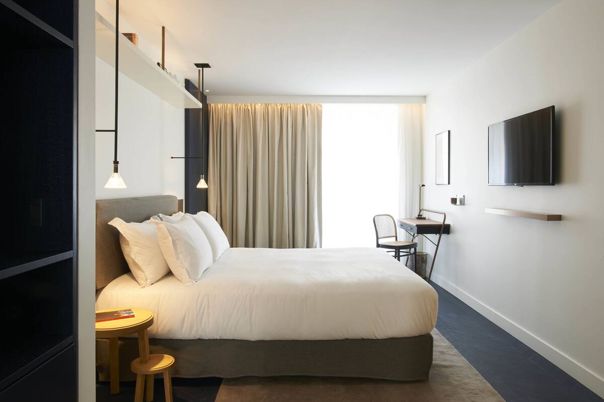 Una habitación de hotel moderna con una cama grande, un escritorio, una silla y un televisor montado en la pared.
