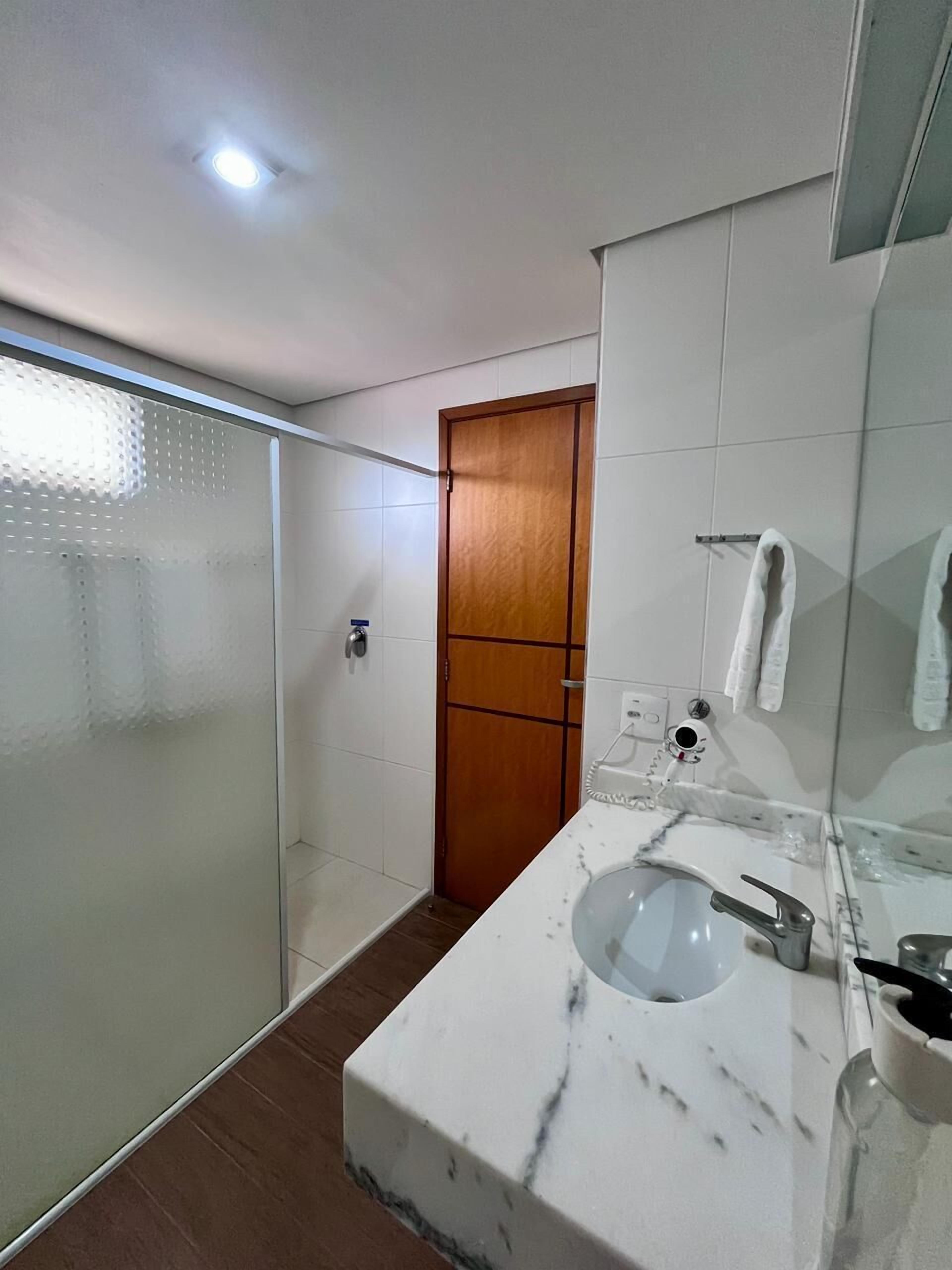 A modern bathroom with a glass shower enclosure, a wooden door, a marble sink, and a towel rack.