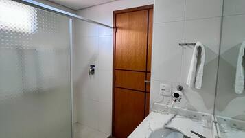 A modern bathroom with a glass shower enclosure, a wooden door, a marble sink, and a towel rack.