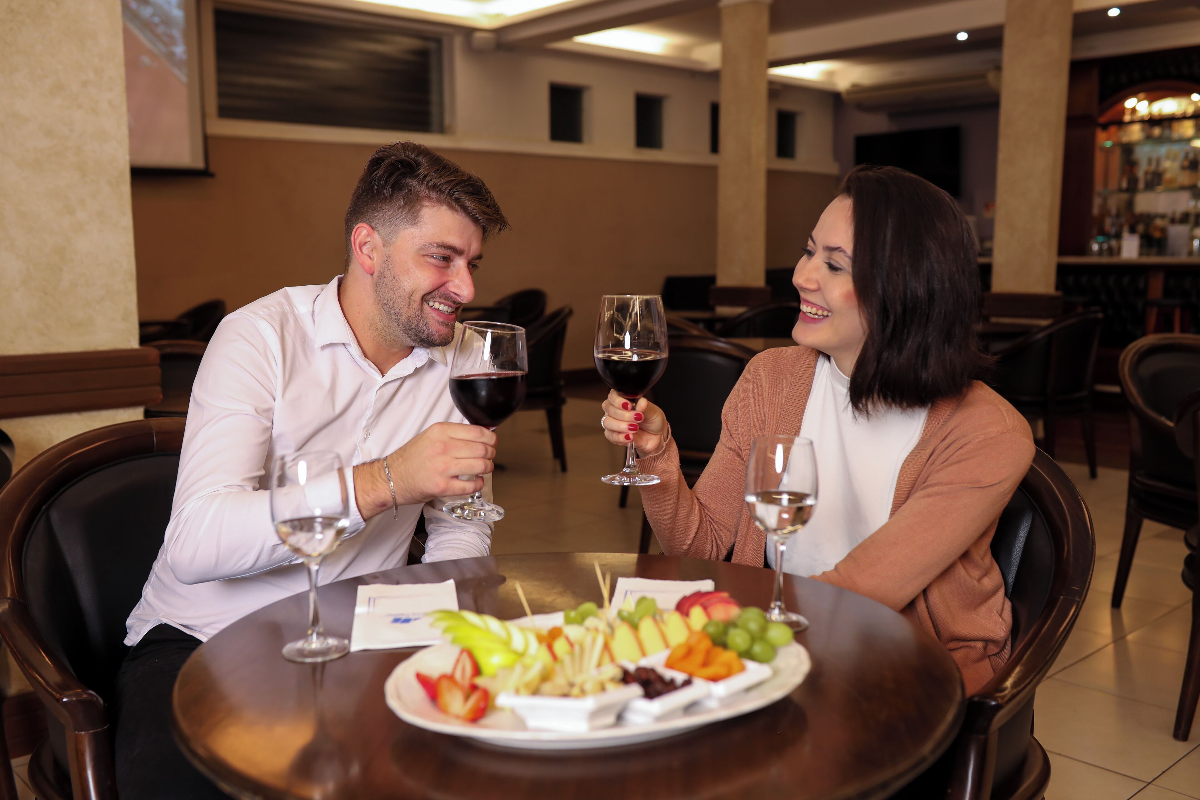 A couple seated at a round table with a fruit platter and wine glasses.