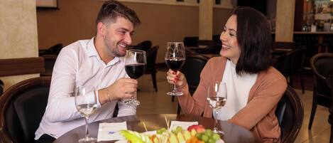 A couple seated at a round table with a fruit platter and wine glasses.