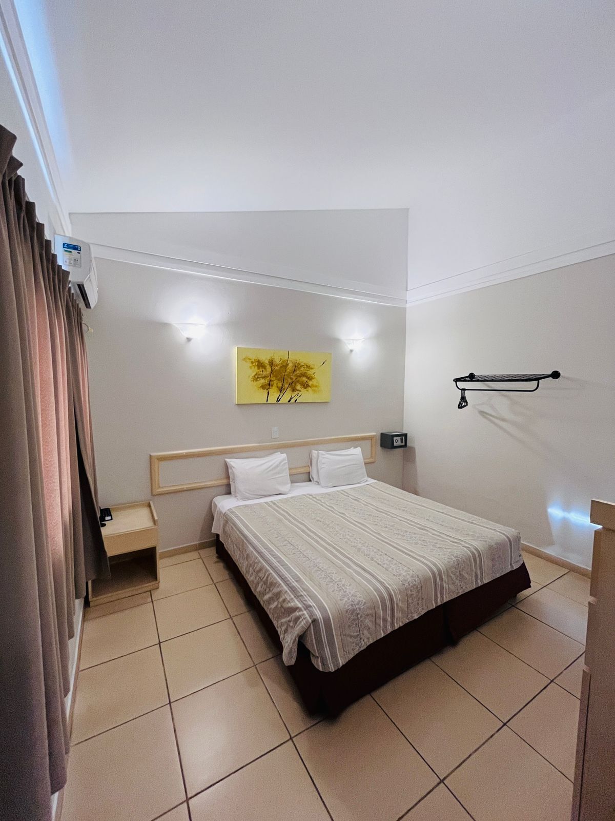 A neatly arranged bedroom with a bed, bedside tables, a wall-mounted shelf, and a painting.