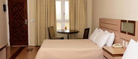 Una habitación de hotel con dos camas, una mesita, sillas, una ventana con cortinas y una puerta.