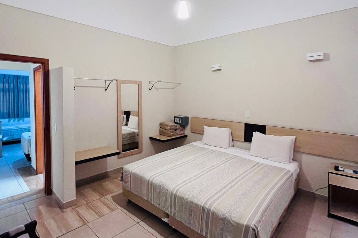 A hotel room with a large bed, a bedside table, a chair, a wardrobe, and a mirror.