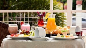 A breakfast setup with various drinks, fruits, pastries, and a glass of orange juice on a table outside.