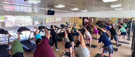 A group of people exercising in a gym with treadmills and mats.