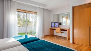 Hotellihuone, jossa on kaksi sänkyä, työpöytä, televisio ja liukuovi, joka johtaa ulos.