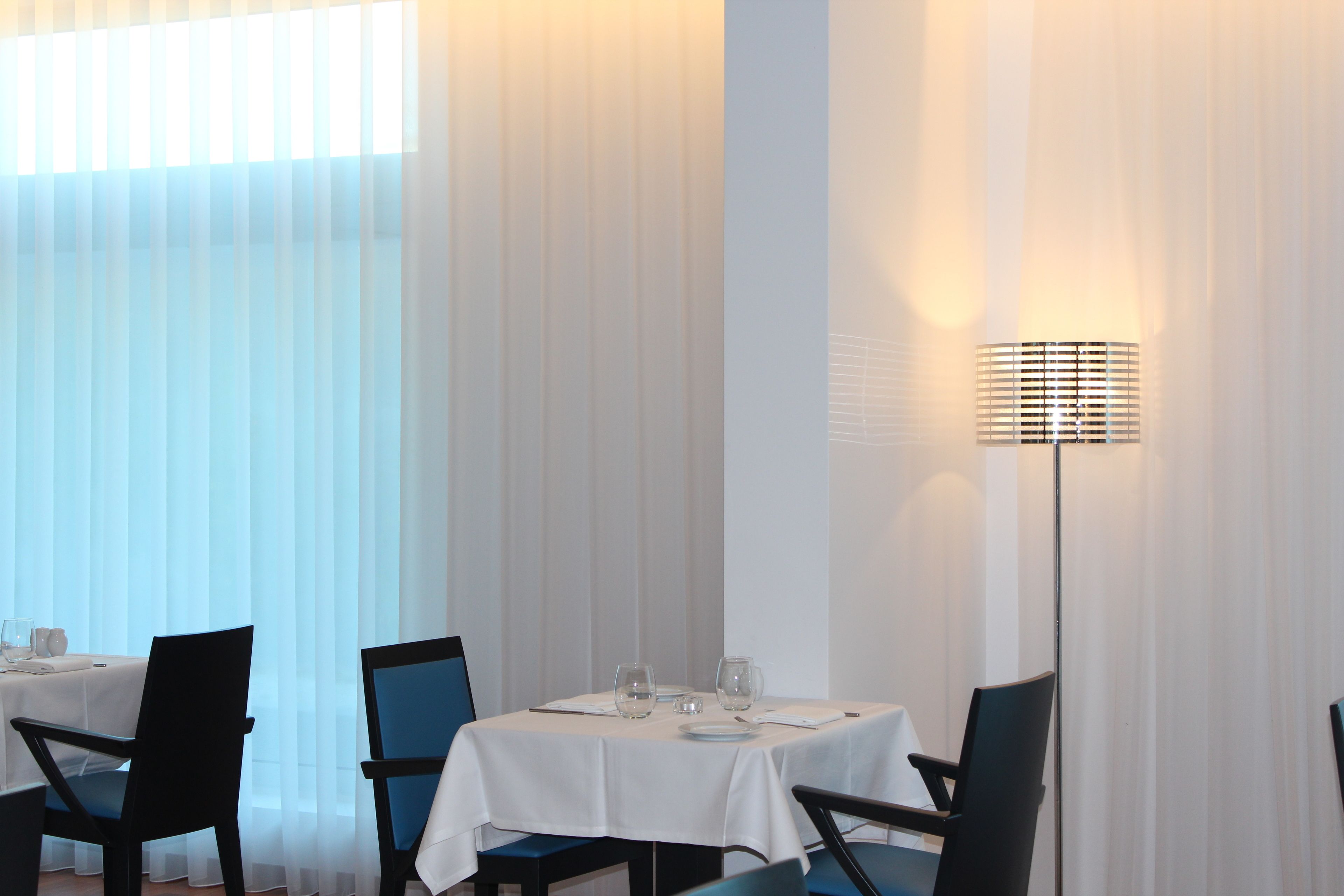 A dining area with a table set for two, featuring a white tablecloth, two chairs, and a floor lamp.