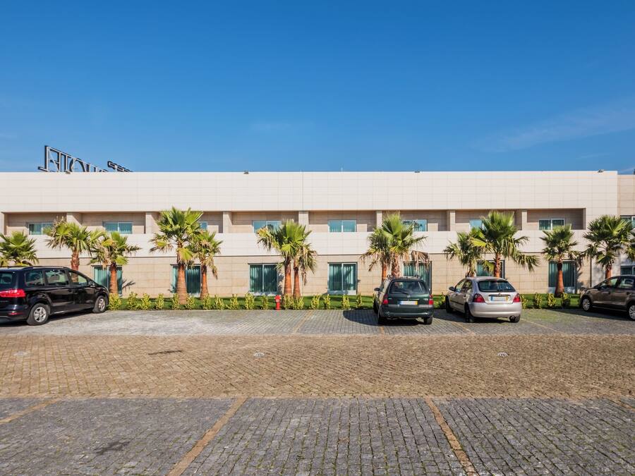 A modern building with a parking lot, palm trees, and a clear sky.