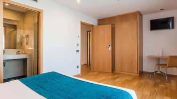 Une chambre d’hôtel avec un lit, une salle de bain avec douche, un bureau avec une chaise et un téléviseur fixé au mur.
