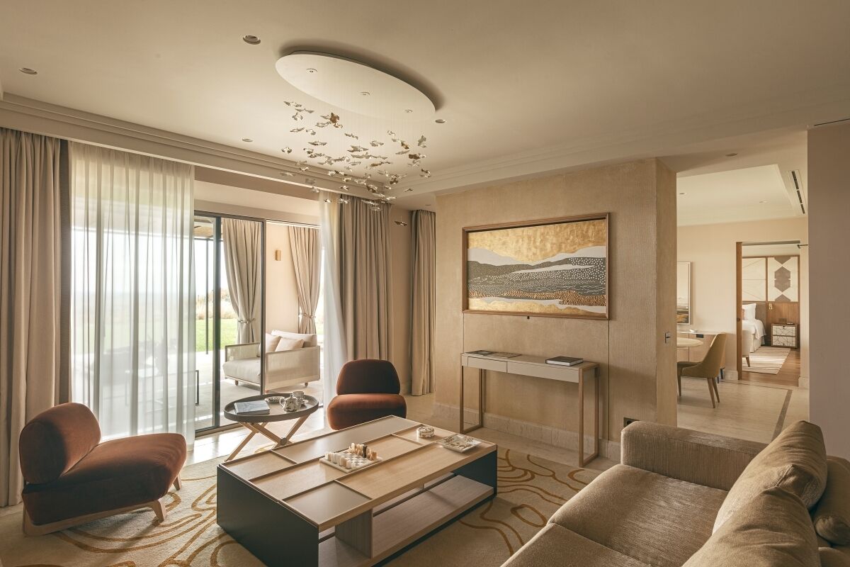 Habitación de hotel moderna con un ventanal grande, un sofá, una mesita de centro y un cuadro en la pared.