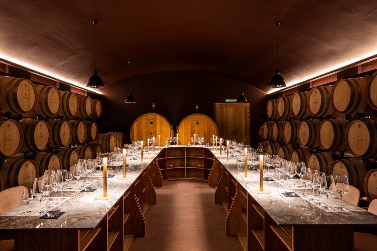 A wine tasting room with a long table set for guests, surrounded by wooden wine barrels.