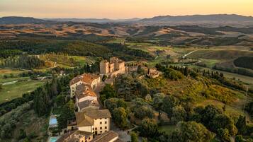 A historic building complex with multiple structures, surrounded by lush greenery and rolling hills.