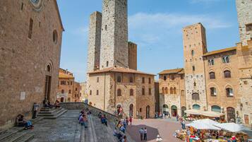 A historic square with stone buildings, a central staircase, and outdoor market stalls.