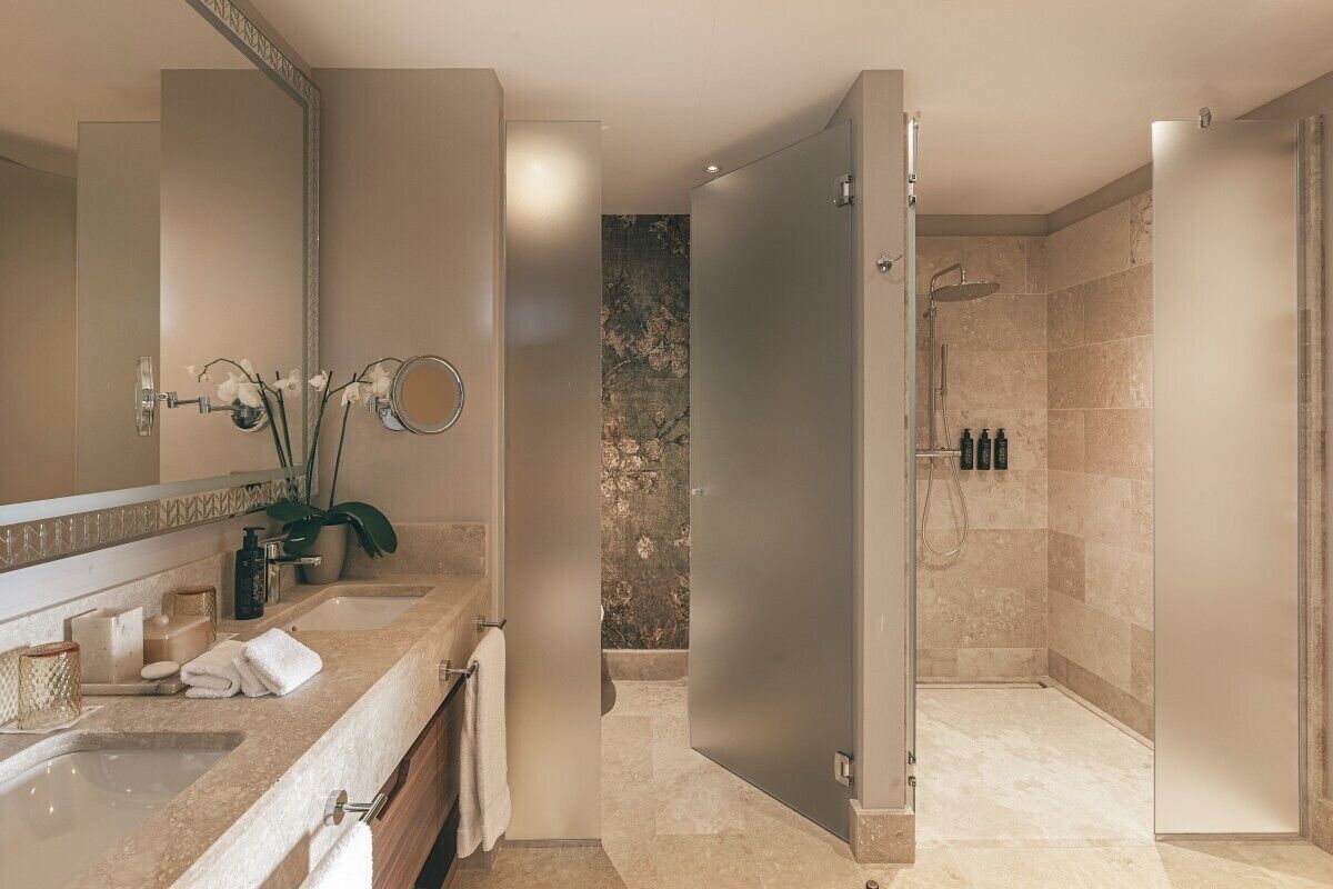 A modern bathroom with a large mirror, two sinks, a shower area, and a decorative wall.