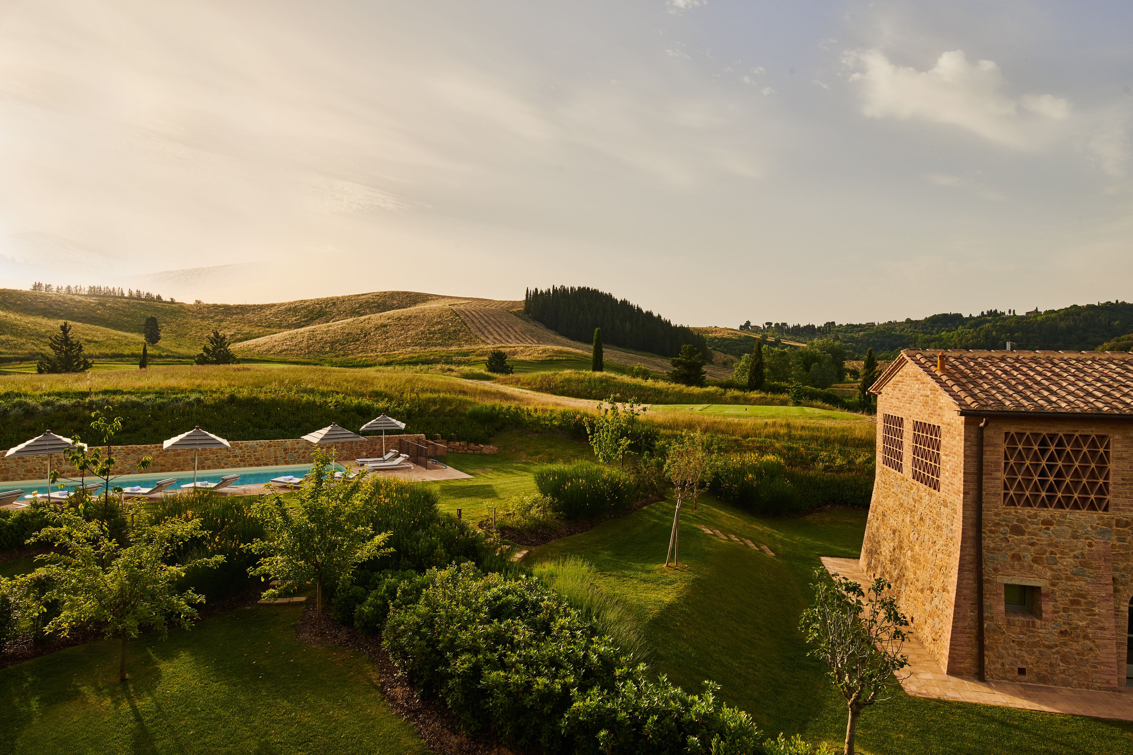 A landscaped garden with a pool, stone building, and rolling hills in the background.
