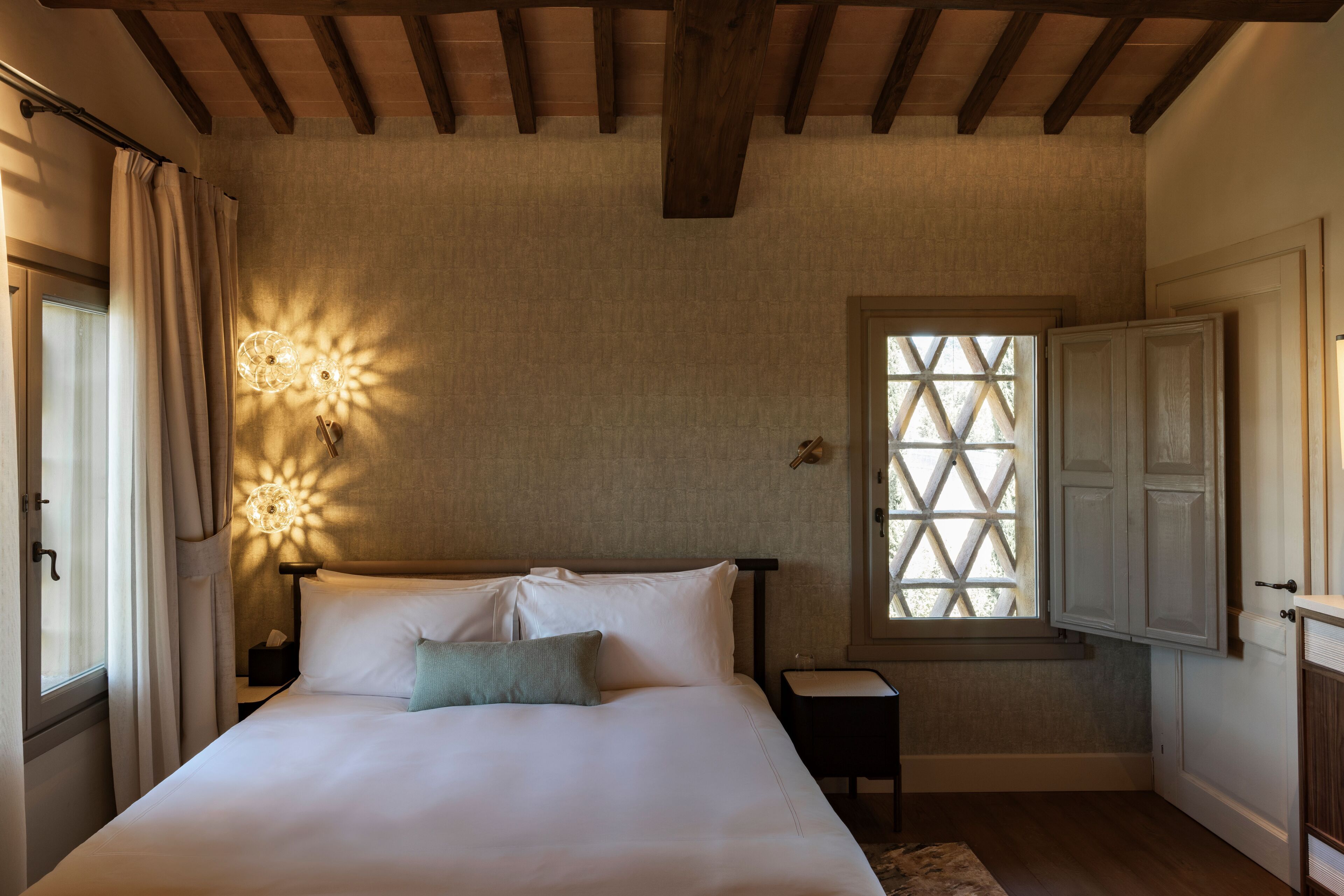 A bedroom with a bed, a nightstand, a window with a lattice design, and a wooden ceiling.