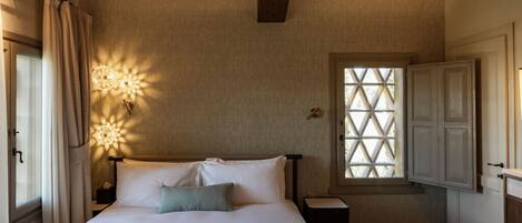 A bedroom with a bed, a nightstand, a window with a lattice design, and a wooden ceiling.