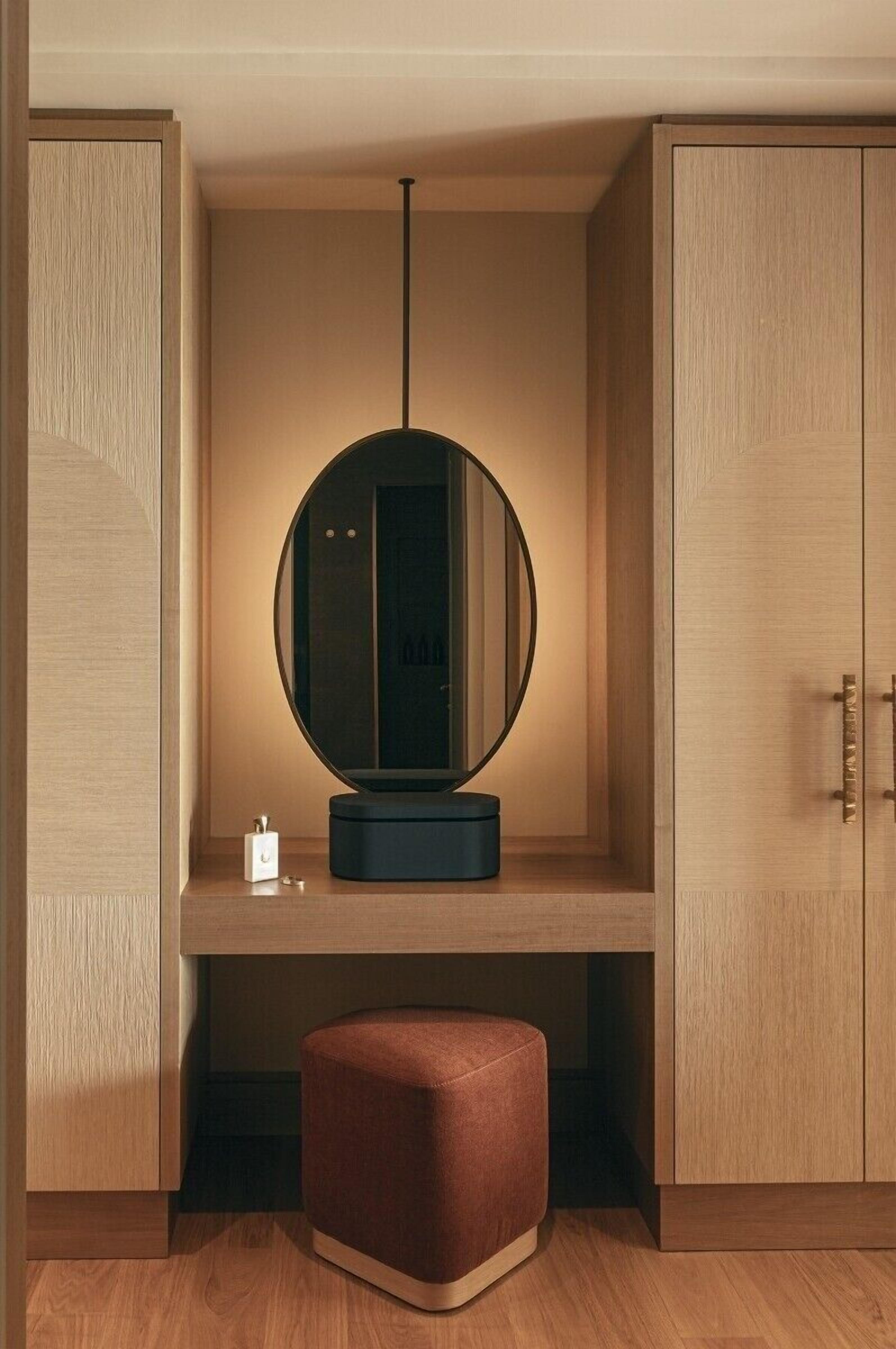 Een moderne wastafel met een ronde spiegel, een klein krukje en een kastje.
