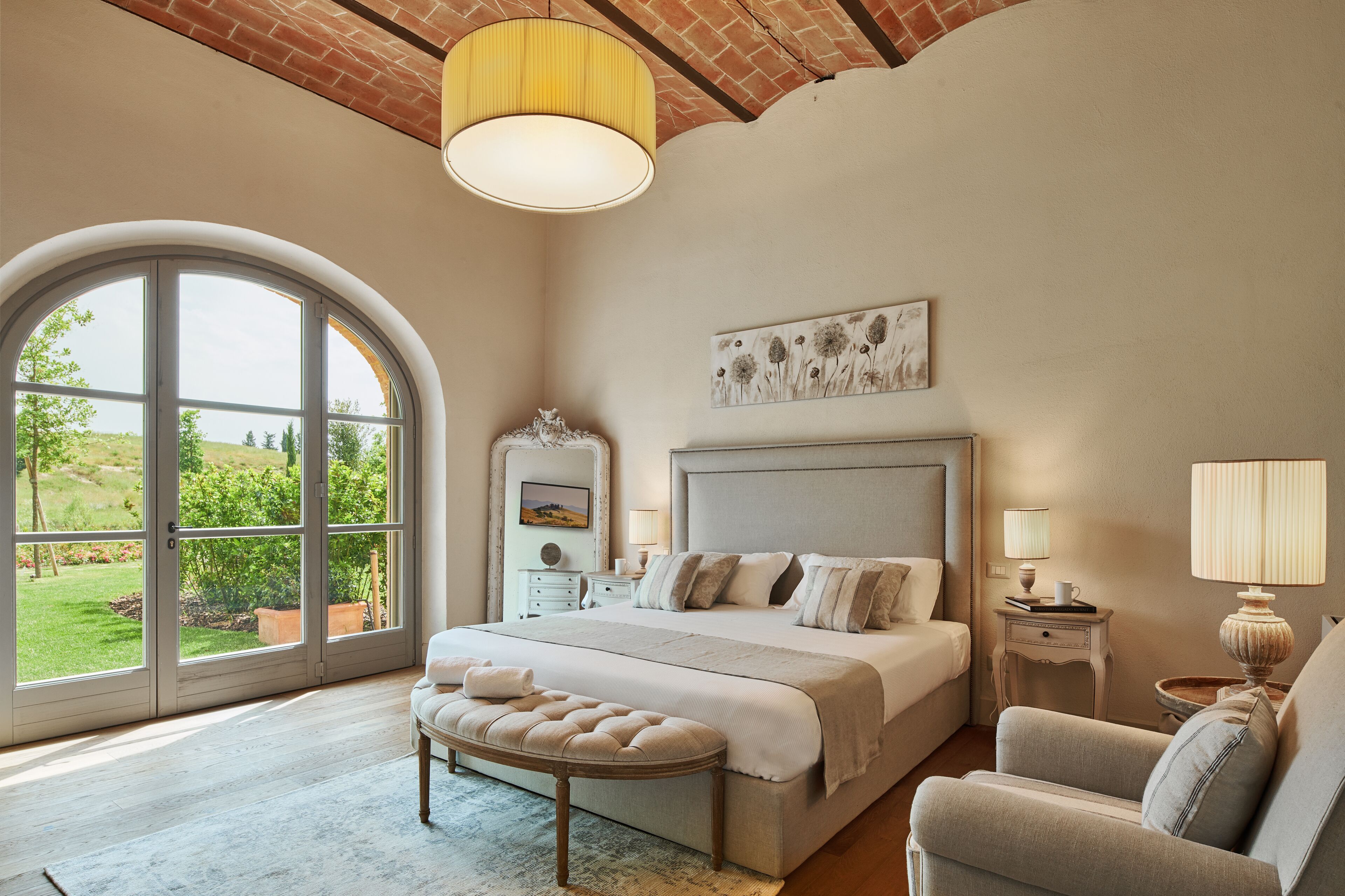 Ein Schlafzimmer mit einem großen Bett, einer Bank, einem Sessel, einem Nachttisch und einer Lampe.