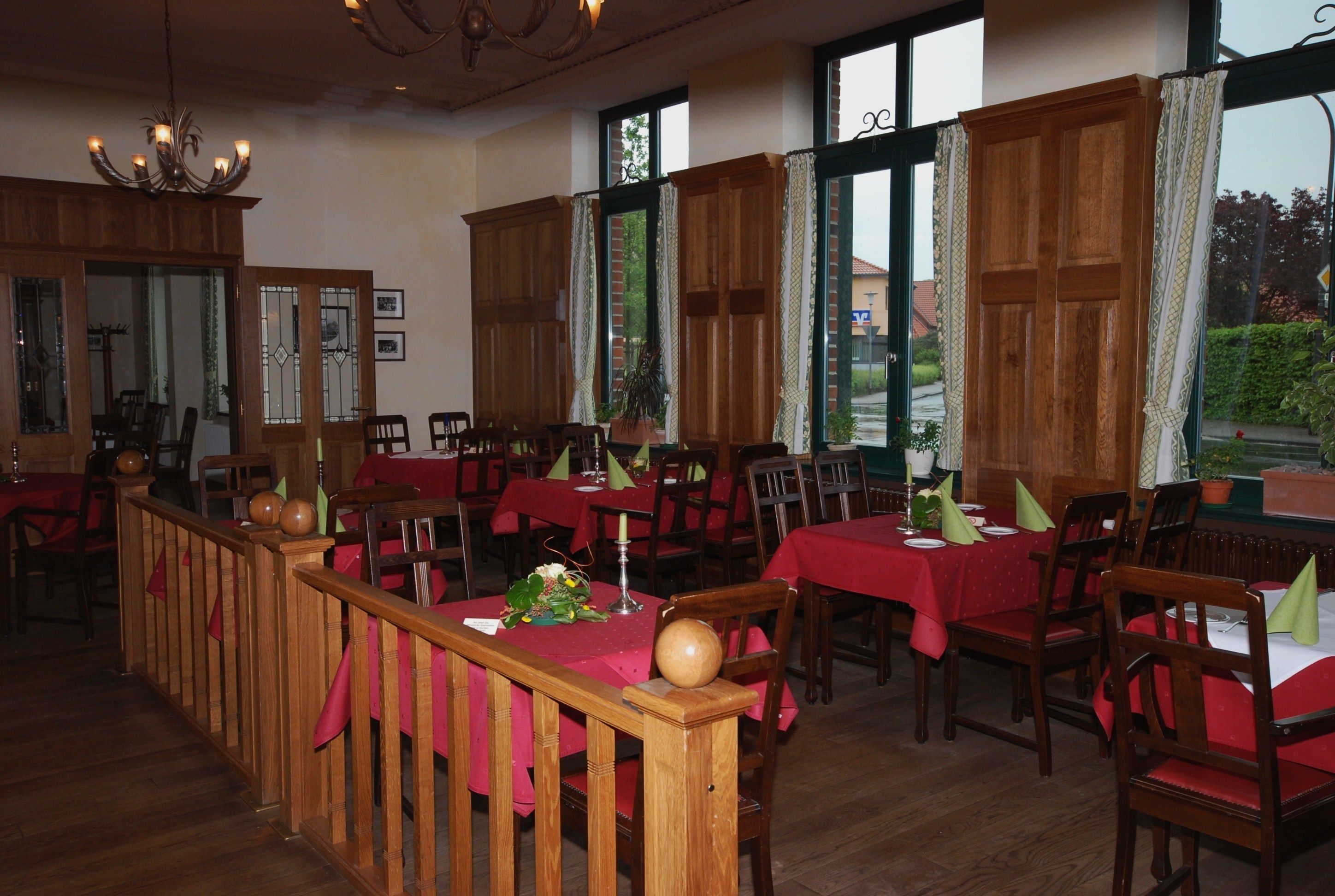 Un restaurante con muebles de madera, manteles rojos y ventanas amplias con cortinas.