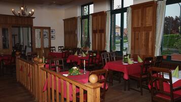 Un restaurante con muebles de madera, manteles rojos y ventanas amplias con cortinas.