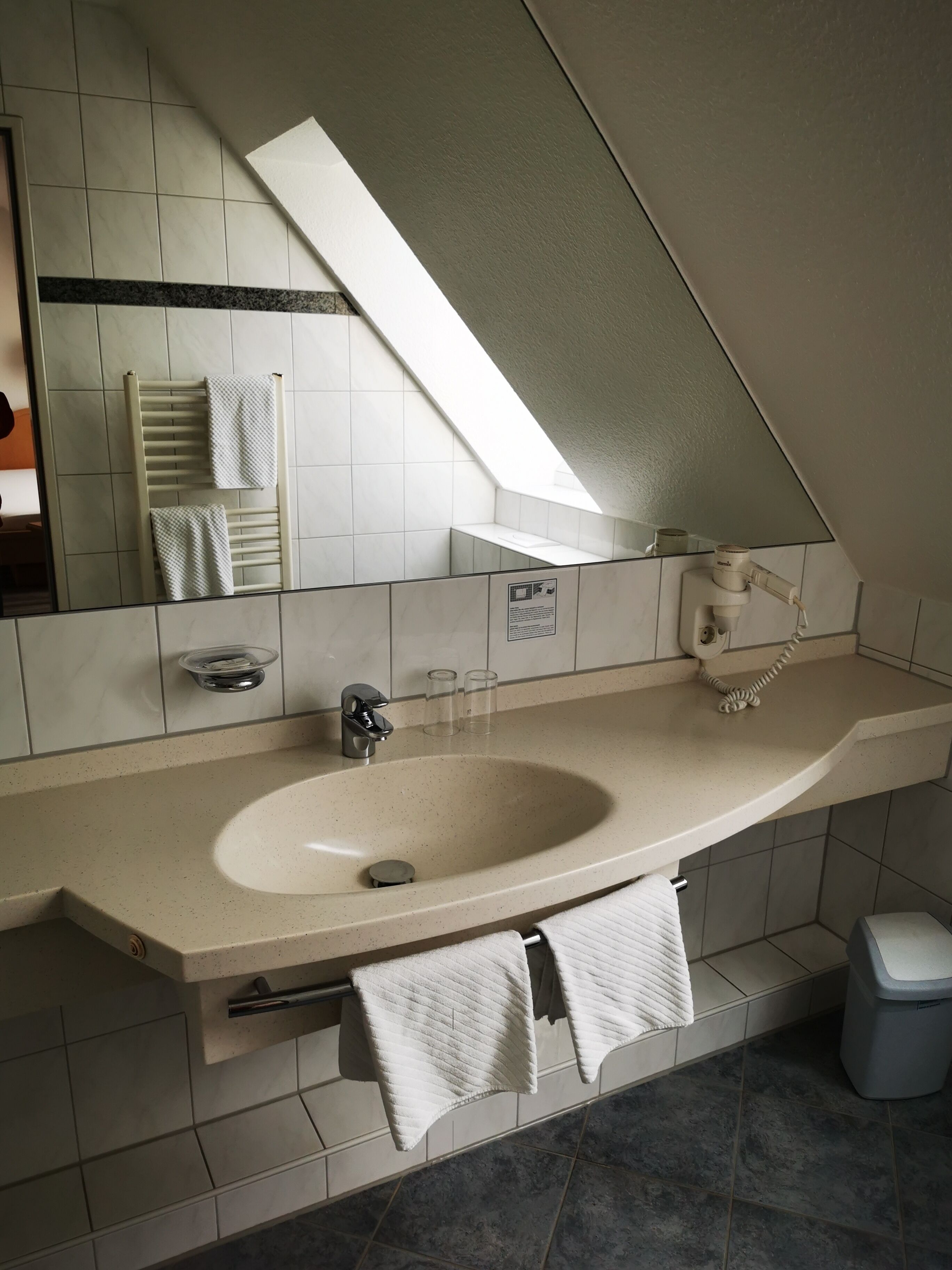 A modern bathroom with a large sink, a mirror, a towel rack, and a shower.