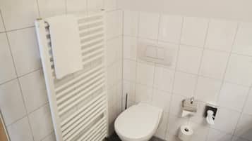 Un baño pequeño y limpio con inodoro blanco, un perchero y un dispensador de toallas de papel.