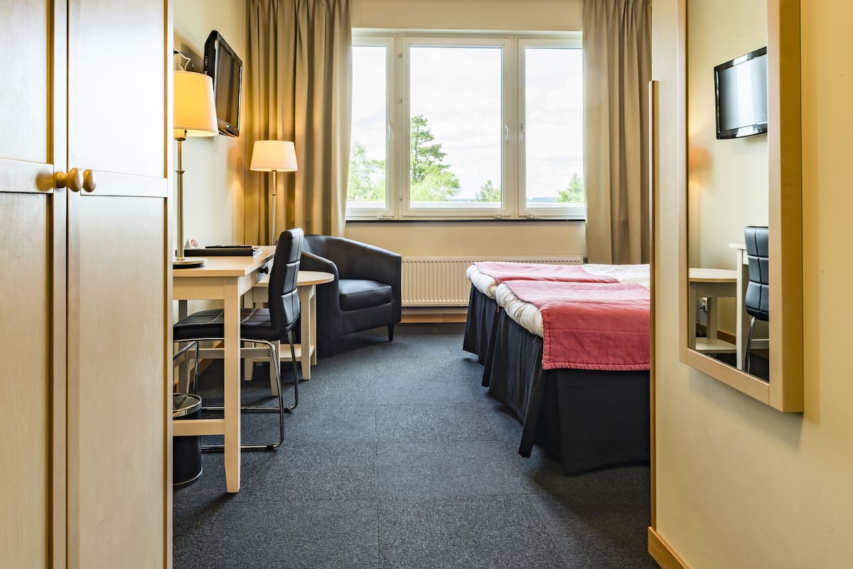 A hotel room with a bed, desk, chair, lamp, and TV.